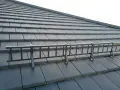 Metalowa drabinka śniegowa na ciemnej dachówce karpiówce w łuskę.