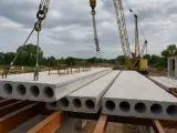 Strop z płyty żerańskiej jest podnoszony przez dźwig na budowie. W tle widać inne płyty i konstrukcje budowlane.