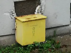 Żółta skrzynka gazowa w elewacji budynku, z napisem "UWAGA GAZ".