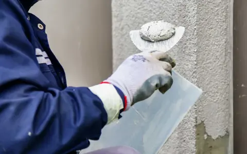 Pracownik w rękawicach nakłada tynk na ścianę. Poznaj atrakcyjną tynkowanie elewacji cenę.