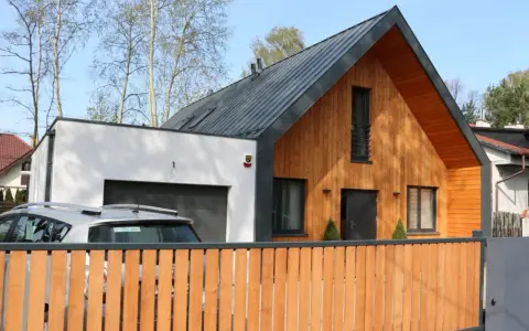 Nowoczesny dom z drewnianą dobudówką do części murowanej. Obok garaż, przed którym stoi samochód.