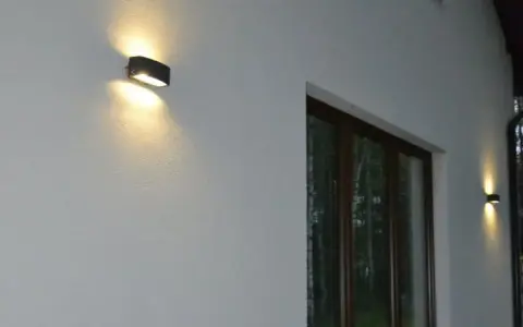 Nierówności na elewacji pod światło, podkreślone przez dwa kinkietowe punkty świetlne.