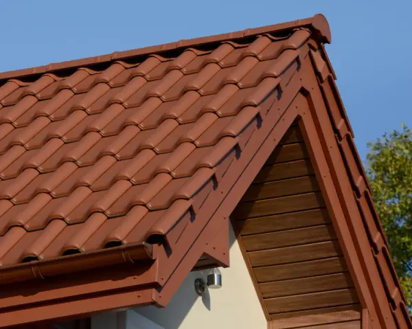 Brązowa, lekka konstrukcja dachu z dachówki ceramicznej, z widocznym okapem i drewnianą podbitką.