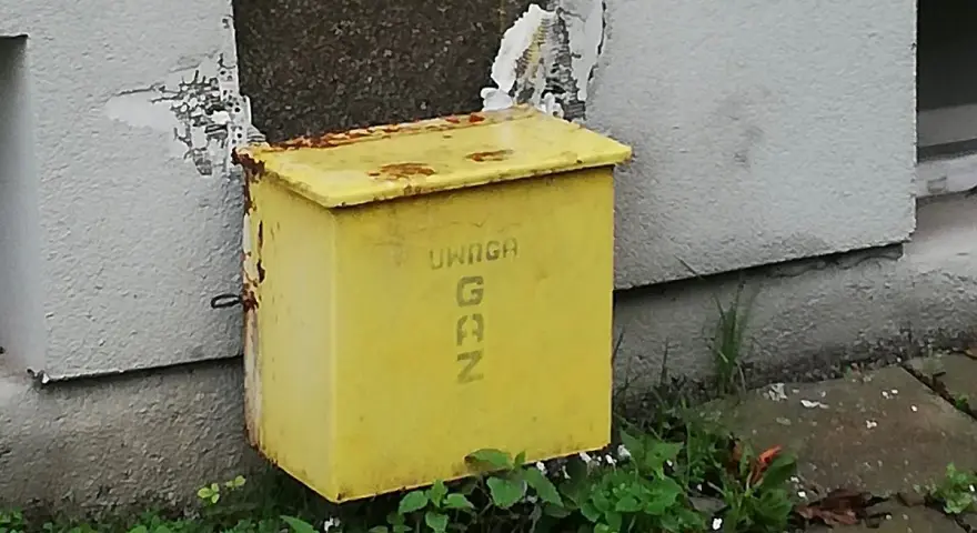 Żółta skrzynka gazowa w elewacji budynku, z napisem "UWAGA GAZ".