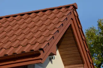 Brązowa, lekka konstrukcja dachu z dachówki ceramicznej, z widocznym okapem i drewnianą podbitką.